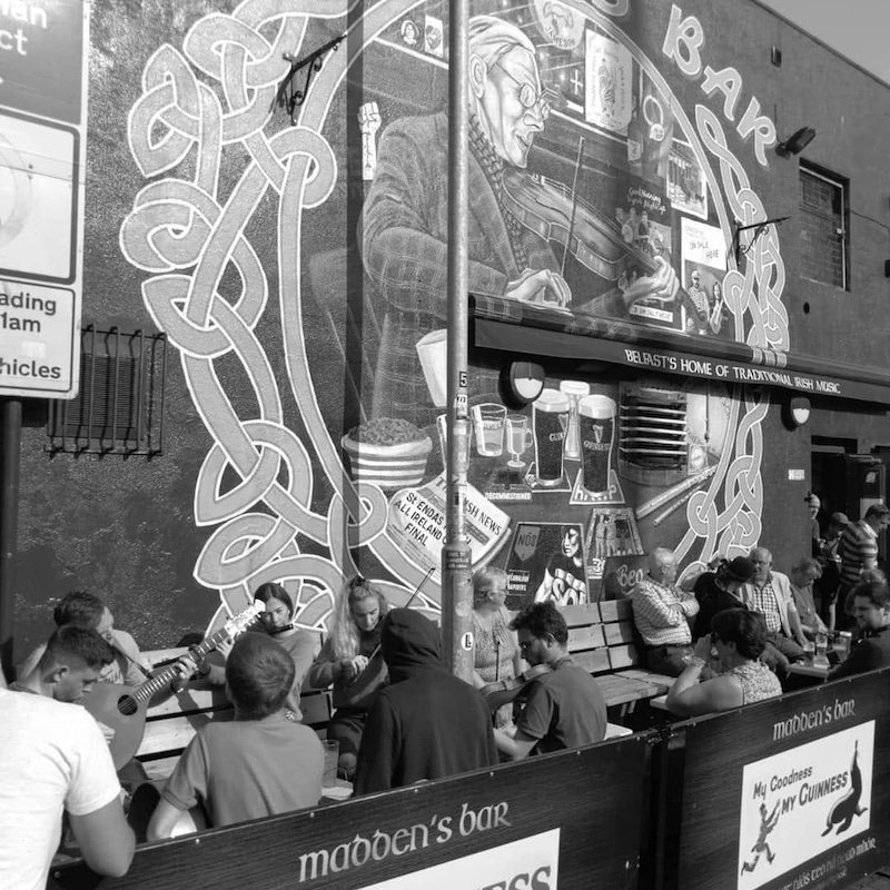 What better place to kick off Belfast Traditional Music Trail than in the legendary Maddens Bar, home of trad music! A visual landmark in itself with its beautiful coloured Celtic-style graffiti, it has welcomed hundreds of both musical legends and beginners from all parts of the world for over 50 years. Step inside Maddens, step inside a world where the living tradition subsist… We strongly advise on treating yourself with a refreshment at the bar downstairs before making your way up the back stairs to the old wooden-floored room to meet with your guides…